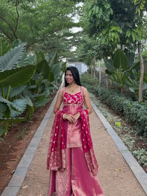 A bridesmaid in a rani pink silk set on a garden path